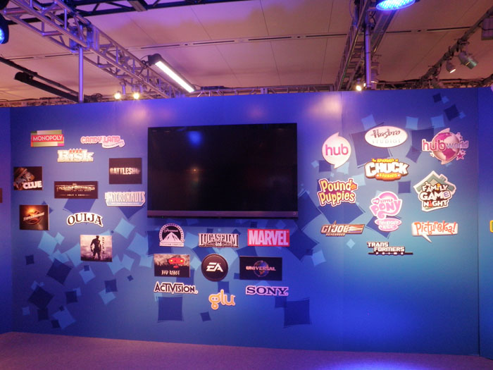 The wall facing the entrance to the downstairs showroom displayed the logos of all of Hasbro's featured brands.